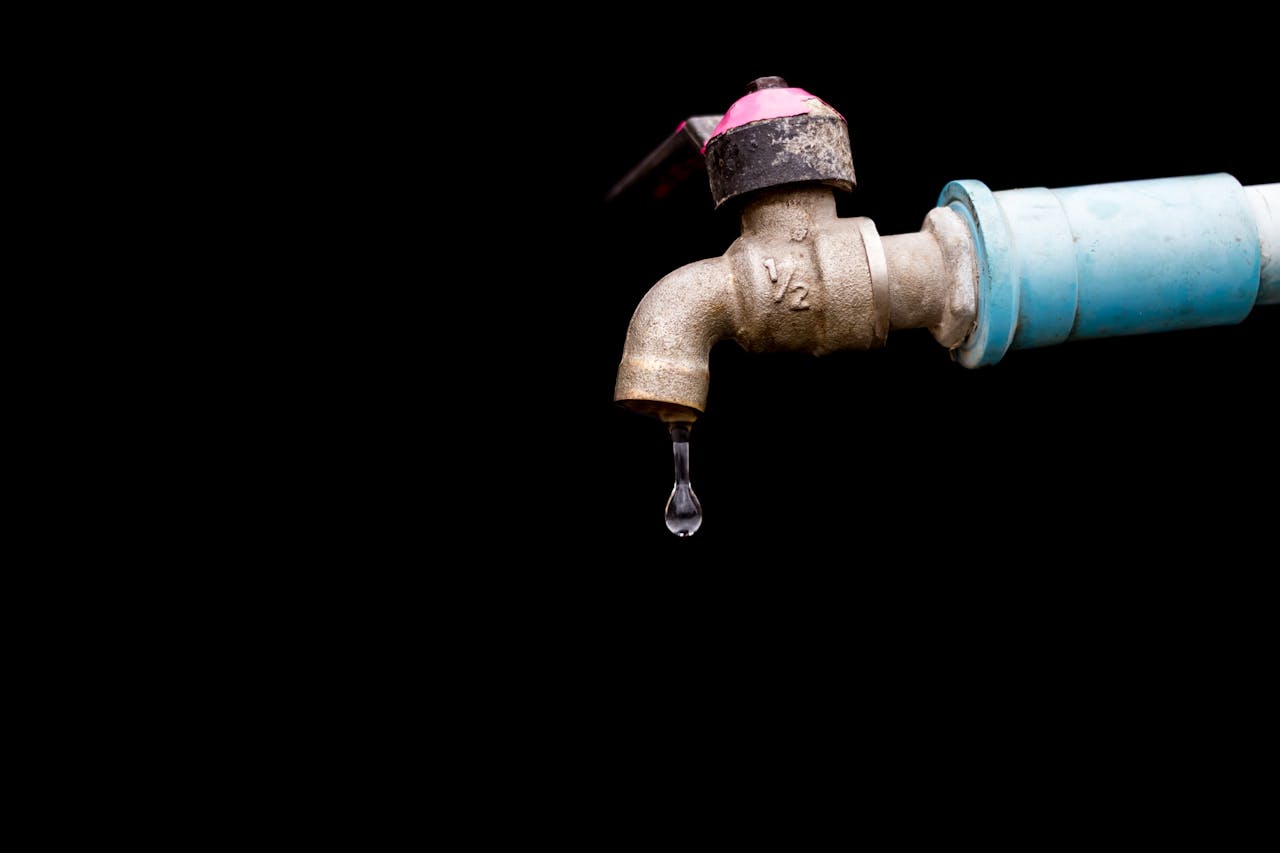 A detailed view of a metal faucet with a single water drop against a black background.
